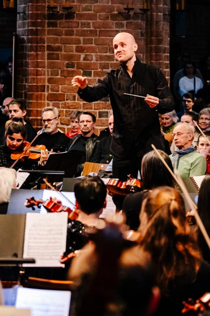 Dirigent vor Orchester, im Hintergrund Publikum