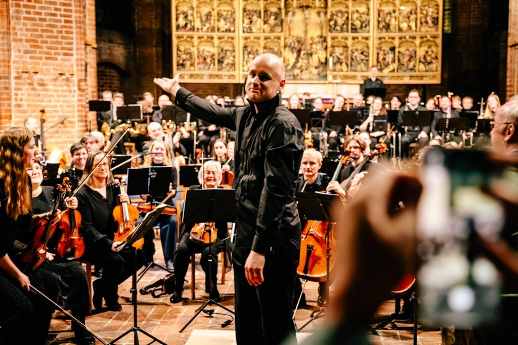 Orchester in einer Kirche, im Vordergrund der Dirigent
